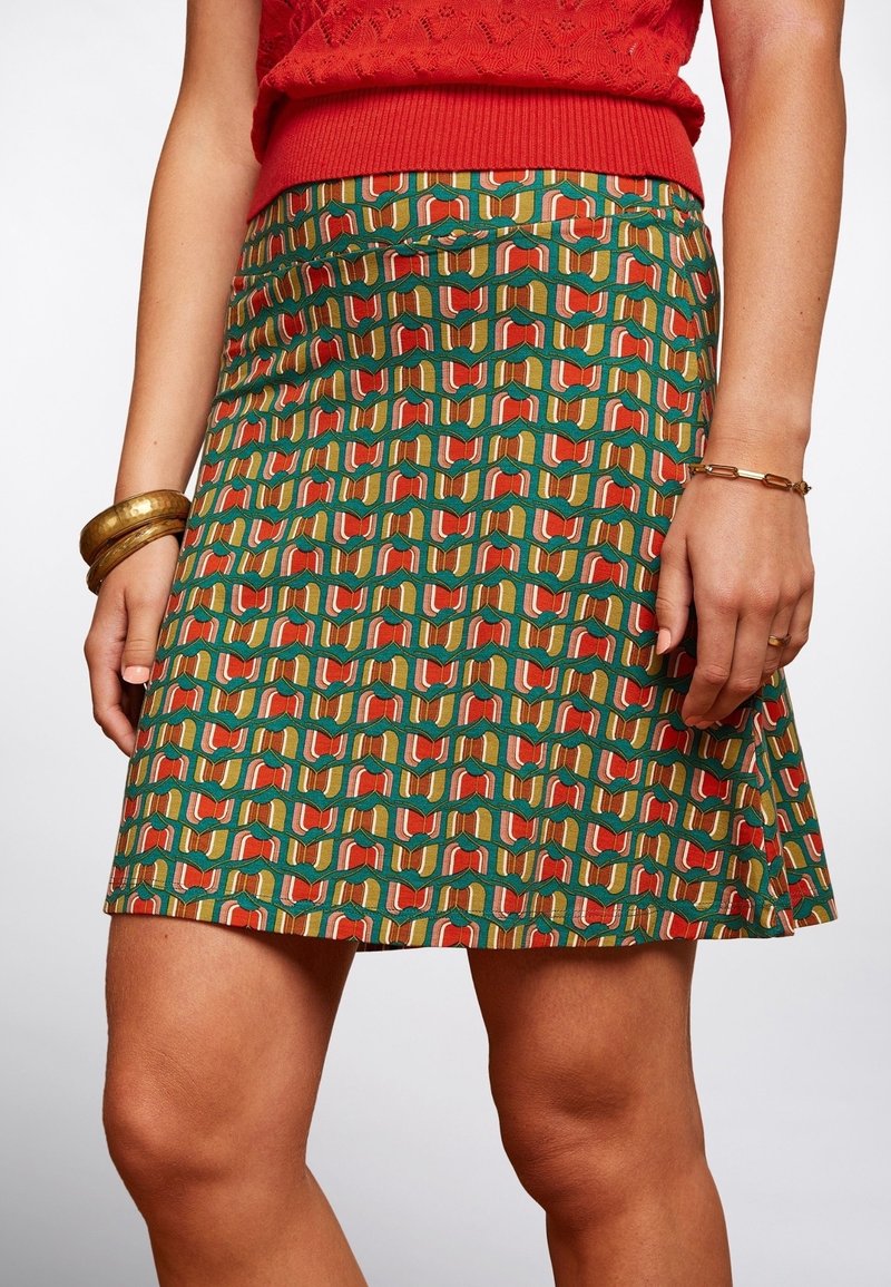 Grön kjol med ett geometriskt mönster av röda, orange och krämfärgade former; tillverkad av ett tyg med en mjuk textur; knälång design.