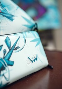 Modrá a bílá grafická peněženka s abstraktními vzory, hladkým syntetickým materiálem, zipovým uzávěrem a stříbrným logem.