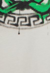Tejido blanco con un diseño gráfico en verde y negro, con un patrón circular y un motivo de clave griega en la parte inferior. Textura sutil visible.