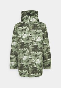 Zöld árnyalatú, kamuflázs mintás dzseki, magas gallérral, kapucnival, patentgombokkal és laza szabással. Vízálló anyagból készült.