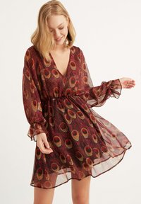 Rotes und schwarzes durchsichtiges Kleid mit V-Ausschnitt, elastischem Bund, langen puffärmel und einem Muster aus goldenen und orangefarbenen Pfauenfedern.