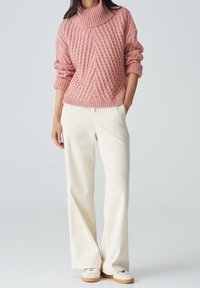 Różowy sweter dzianinowy o fakturze z wysokim kołnierzem, w zestawie z kremowymi spodniami dzwonami z sztruksu i białymi trampkami. Prosty i luźny krój.
