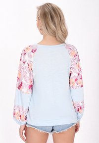 Top azzurro chiaro a maniche lunghe con texture a coste, maniche decorate con un motivo floreale nei toni del rosa e del pesco, scollatura rotonda e vestibilità rilassata.