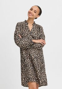 Leopardmönstrad klänning med lös passform, långa ärmar och knäppt krage. Mjuk tyg, knä-lång och med något rundad fåll.