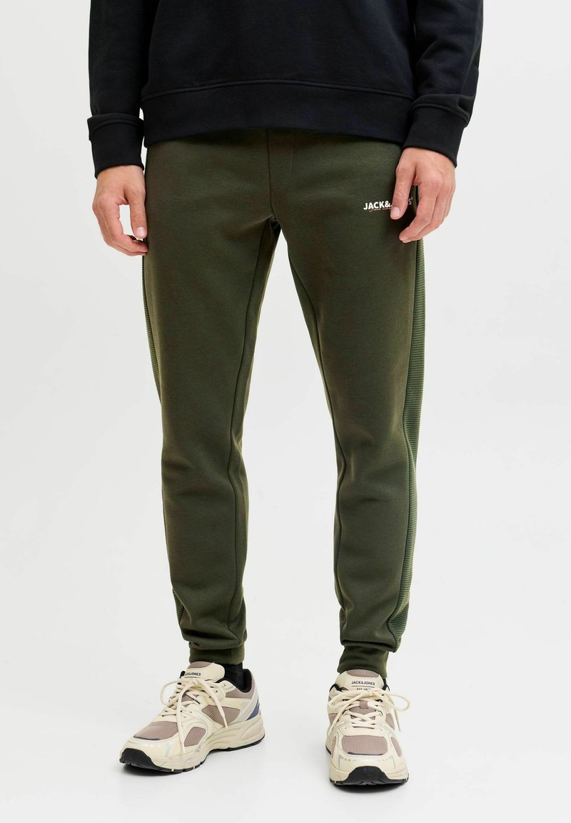 Grønne sweatpants med slim fit, der har en sidestregtekstur, elastisk talje og et lille logo på fronten. Sammen med beige sneakers.