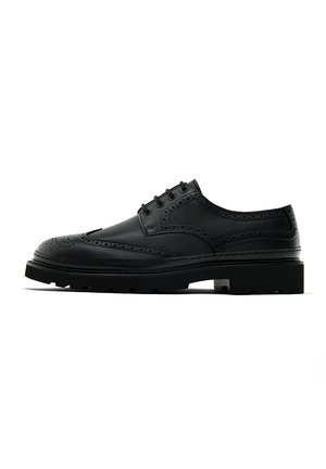 Black leather brogue shoe with perforated detailing, round toe, and a thick sole. Features five eyelets and a smooth finish.