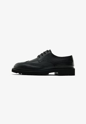 Chaussure brogue en cuir noir avec des détails perforés, bout rond et semelle épaisse. Comprend cinq œillets et une finition lisse.