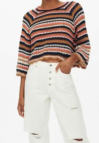 Häkelpullover mit mehrfarbigen horizontalen Streifen, mit rundem Ausschnitt und gezacktem Saum. Kombiniert mit weißen, hoch taillierten Jeans.