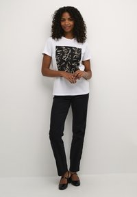 T-shirt blanche à manches courtes avec un motif floral noir, associée à un pantalon noir et des chaussures noires. Ajustement simple et décontracté.