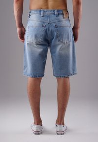 Denim shorts in light blue wash with a faded effect, five-pocket design, and a leather patch on the back waistband. Worn with white sneakers.