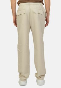 Pantaloni beige realizzati in un tessuto leggero presentano una vestibilità rilassata, vita elastica e tasche posteriori con bottone. Indossati con sneakers bianche.