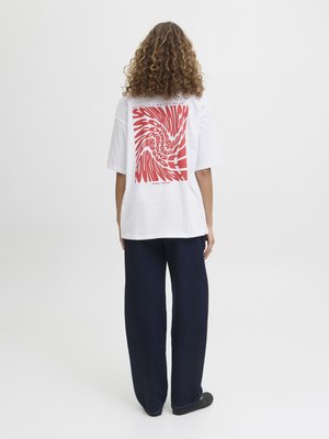 T-shirt blanc oversize avec un graphisme en spirale rouge au dos. Assortie à un pantalon large sombre. Texture de tissu lisse et coupe décontractée.