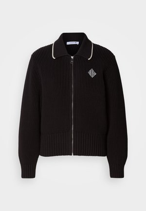 Black knitted jacket with ribbed texture, zip closure, contrasting cream collar, and a small logo detail on the chest.