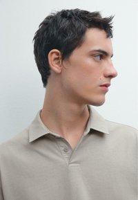 Beige polo shirt met een kraag, twee-knopen sluiting en een zachte textuur. Schoon ontwerp met een subtiele gestikte detail nabij de halslijn.
