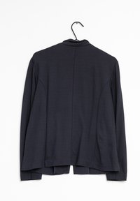 Blazer long gris foncé à manches longues avec une texture douce et lisse. Il possède une coupe lég èrement ajustée et un col montant, suspendu à un crochet noir.