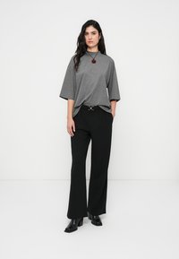 Γκρι τοπ με κοντά μανίκια και ψηλό λαιμό, συνδυασμένο με μαύρο παντελόνι φαρδιάς γραμμής και μαύρη ζώνη με χρυσή κυκλική λεπτομέρεια.