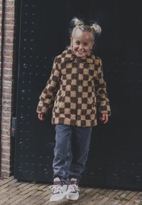 Bruine en beige geblokte fleece jack met een rits aan de voorkant, gedragen over grijze broek en witte sneakers. Gelaagd oppervlak, gezellige ontwerp.