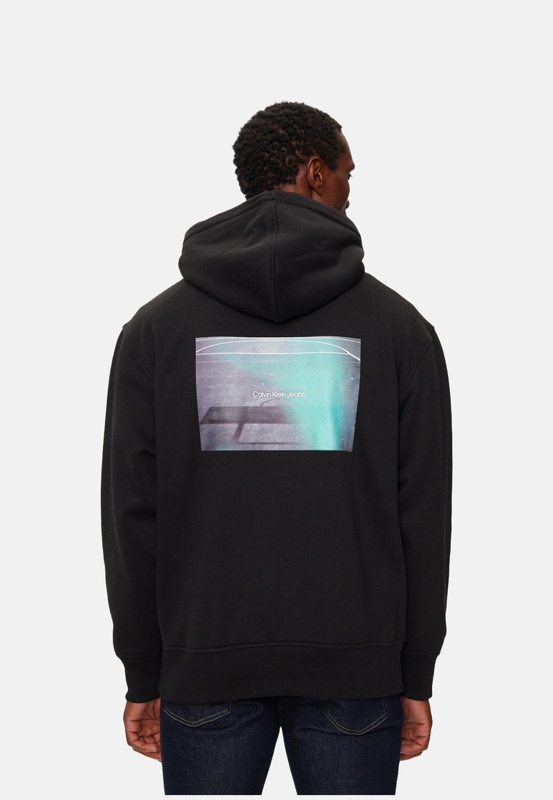 Sudadera negra con capucha que presenta un estampado gráfico en la parte posterior. El material es una mezcla de algodón. El estampado incluye texto y un diseño abstracto en tonos azules y grises.