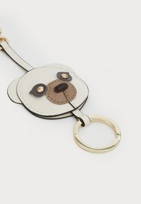 Porte-clés avec un design d'ours, un extérieur en cuir crème et des accents marron, une quincaillerie dorée, et un anneau clé rond.