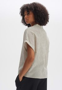 Top corto a maniche corte color beige chiaro con un motivo a coste testurizzato. Vestibilità ampia con collo alto e spalle rilassate, infilato in pantaloni scuri.