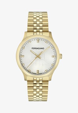 Reloj dorado con esfera plateada texturizada, presenta marcadores de hora de cristal y manecillas doradas, sobre una pulsera de eslabones dorados. Logo mostrado de manera destacada.