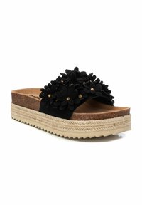 Chanclas negras con apliques de fieltro florales y tachuelas doradas en la correa. Plantilla de corcho y suela de goma beige texturizada con acentos de yute.