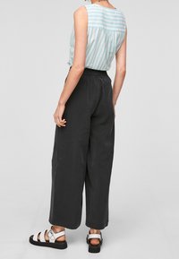 Top senza maniche a righe blu chiaro, pantaloni neri larghi e morbidi, e sandali bianchi con cinturini. Design su misura con dettaglio arricciato sul retro.
