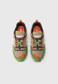 Pár barna és zöld Minecraft témájú tornacipő fekete fűzőkkel, a nyelvükön pixeles Creeper arcdíszítéssel.