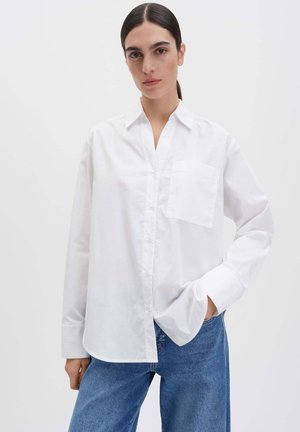 Weißes Hemd aus Baumwolle mit klassischem Kragen, langen Ärmeln, Brusttasche und lockerem Schnitt, kombiniert mit blauen Jeans.