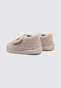 Zapatillas de casa marrones y esponjosas con un upper texturizado, suela de goma beige y un botón decorativo en un lado. Diseñadas para la comodidad.