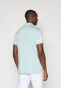 Lys blå polo skjorte med kort krage, sidesplitter, og hvite striper på ermene. Glatt tekstur og tettsittende design.