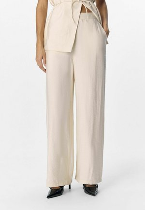 Pantalons larges beige en tissu lisse avec une texture subtile. Présentent des poches latérales et une silhouette décontractée pour plus de confort.