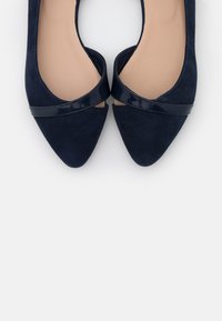 Marineblå flate ballettsko i suede med spiss tå og blank patentlærstropp over vristen. Glatt innvendig fôr og minimalistisk design.
