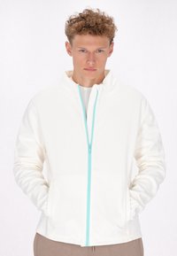 Witte zip-up jas met een hoge kraag en turquoise ritsaccent. Heeft lange mouwen en zijzakken, gemaakt van zacht materiaal.