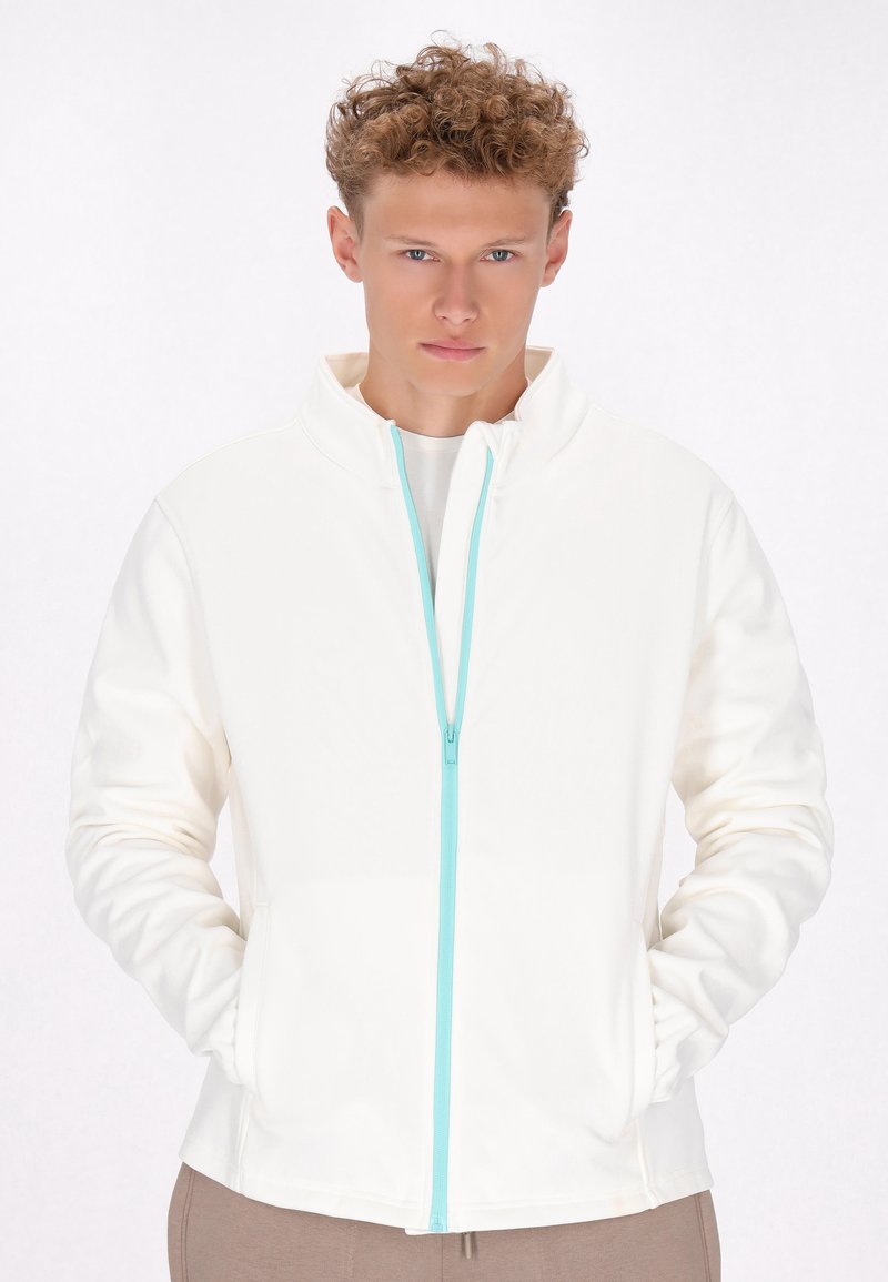 Hvid zip-up jakke med høj krave og turkis lynlåsdetalje. Har lange ærmer og sidelommer, fremstillet af blødt stof.