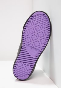 Czarna podeszwa sneakersa z teksturowaną, fioletową gumową spodem, ozdobiona geometrycznymi wzorami oraz wytłoczonym logo "Converse All Star".