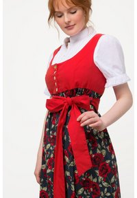 Röd korsettklänning med en vit skjorta under, blommig marinblå kjol, midjeband, guldknappar och korta puffärmar med spetsdetaljer.