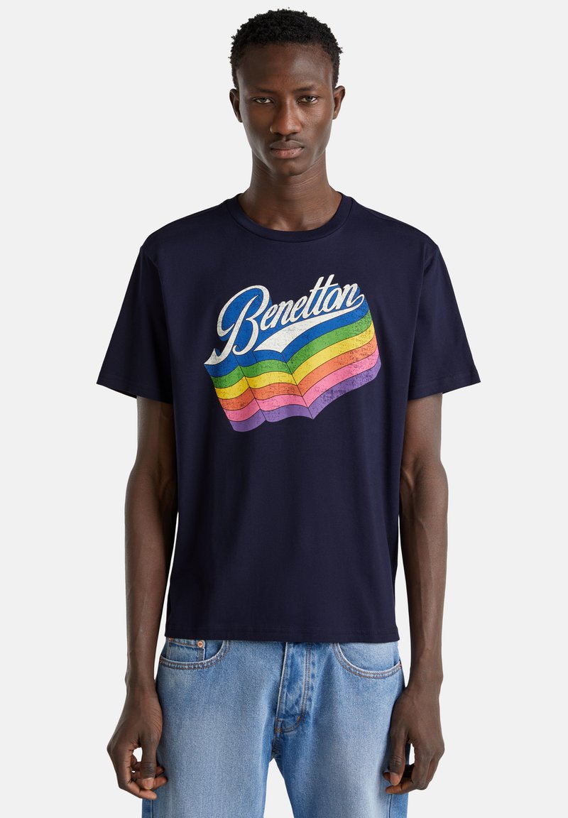 Navy modrý bavlněný tričko s multibarevným retro stylem loga "Benetton" se vlnitými pruhy v růžové, žluté a zelené barvě. Krátké rukávy.
