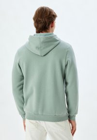 Sudadera verde menta con capucha, puños y dobladillo acanalados. Hecha de material suave, presenta un diseño sencillo sin patrones ni adornos.