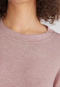 Ljusrosa ribbad tröja med rund halsringning och strukturerad tyg. Kragen har en subtil sömdetalj.