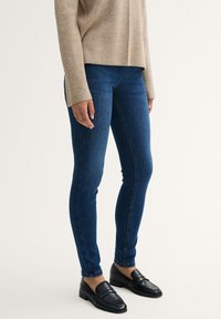 Jeans ajustados de color azul, hechos de denim, que presentan una textura suave y un ligero estiramiento. Combinados con mocasines negros para contrastar.