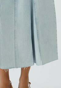 Lichtblauwe denimrok met een uitlopende vorm, onafgewerkte zoom en zichtbare stikseldetails. De stof heeft een licht gestructureerde afwerking.