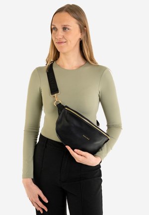 Zwarte leren crossbody tas met een gouden rits en een gouden logo. De strap is gemaakt van zwarte stof met een merknaam. Casual outfit met lange mouwen.