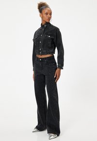 Chaqueta recortada de mezclilla negra con bolsillos frontales, combinada con jeans negros acampanados que presentan detalles de tachuelas plateadas. Zapatos plateados de punta afilada.