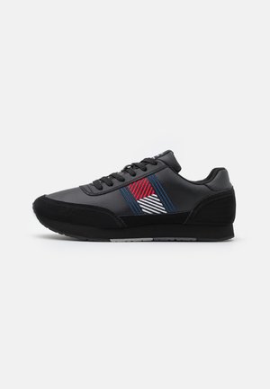 Black athletic shoe with synthetic material, featuring a patterned design with red, white, and blue accents, textured black suede overlays.