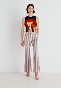 Top noir sans manches avec imprimé abstrait ; pantalon taille haute, évasé avec des rayures verticales multicolores ; sandales à talon carré.