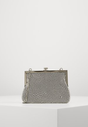 Petit sac de soirée en maille argentée avec cadre métallique, fermoir à clip, et une bandoulière en chaîne argentée posé sur une surface blanche.