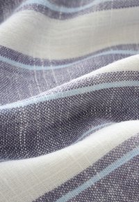 Gros plan d'un tissu texturé avec un motif tissé de rayures horizontales blanches, grises et bleu clair.