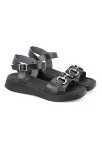 Schwarze Ledersandalen mit verstellbaren Knöchelriemen, Schnallenbeschlägen und flachen Sohlen. Sie verfügen über eine glatte Textur und ein offenes Zehendesign.