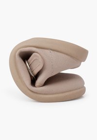 Gefaltete beigefarbene Schuhe mit einem strukturierten Obermaterial aus Stoff und einer glatten Gummisohle, die ein kleines Metallelement aufweist.